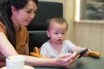 Fototapeta premium Young mother calming her baby with phone inside Japanese sushi restaurant