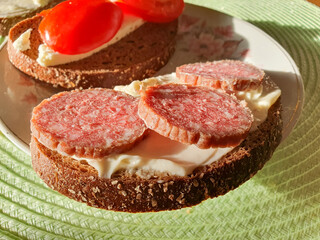 Breakfast on the table: a sandwich with sausage and butter, with cheese and tomatoes on a plate, close-up. Sandwich with sausage.