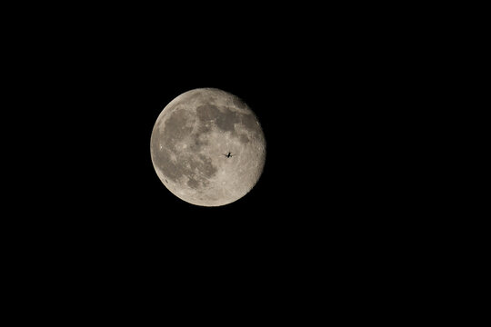 The silhouette of an airplane against the moon. Receding plane against the full moon in the dark night sky.