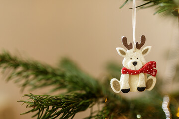 Charming close-up of a handcrafted reindeer Christmas ornament hanging on a lush green fir tree....