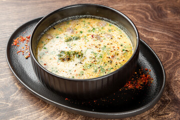 Creamy soup served in a bowl on a black plate, garnished with herbs and spices. Rustic wooden background adds warmth and contrast. Top view, close-up, food styling.