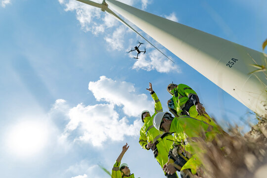 Engineers use a drone to inspect a wind turbine on a bright day, showcasing the integration of technology in renewable energy projects. teamwork, wind power, and modern engineering solutions. - Powered by Adobe