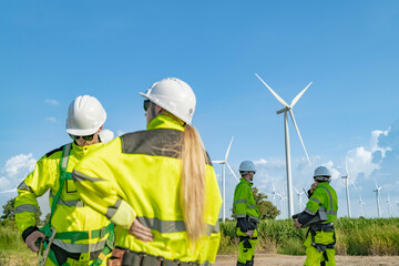 A group of engineers in safety gear work on a wind farm, discussing renewable energy operations....