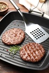 Pan with grilled patties, spices and slotted spatula on wooden table, closeup