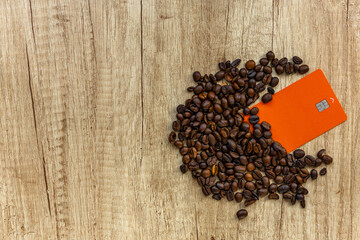 Top view of roasted coffee beans, credit card, and printed chart showing rising global coffee prices on wooden table.