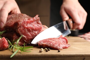 Woman cutting raw beef meat at table, closeup