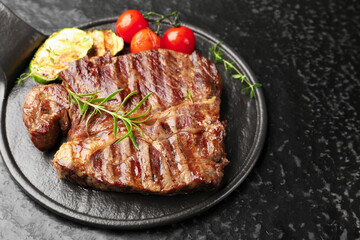 Delicious grilled beef steak with rosemary, zucchini and tomatoes on dark textured table, closeup. Space for text