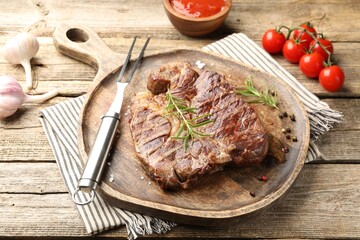 Delicious grilled beef steak with rosemary, spices, carving fork and products on wooden table, closeup