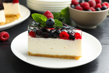 Piece of delicious cheesecake with berries and mint on black wooden table, closeup