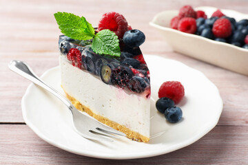 Piece of delicious cheesecake with berries, mint and fork on wooden table, closeup