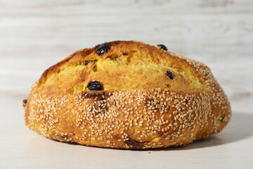 Loaf of fresh bread with sesame seeds and raisins on white wooden table, closeup