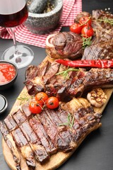 Pieces of tasty grilled beef with rosemary and vegetables on black wooden table, above view
