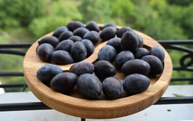 Close-up of fresh dark purple plums on a wooden serving board with soft blurred green nature...