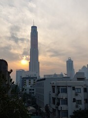 Obraz premium Morning sun rising and hiding behind the high tower building under delicate sky background