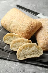 Fresh crispy ciabattas and knife on grey textured table, closeup