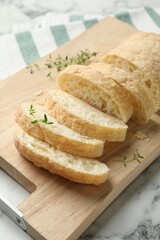 Cut crispy ciabatta and thyme on white marble table, closeup