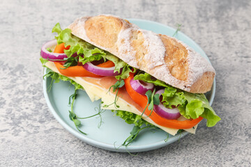 Delicious ciabatta sandwich with prosciutto, cheese and vegetables on light grey table, closeup