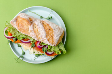 Delicious ciabatta sandwich with prosciutto, cheese and vegetables on green background, top view. Space for text