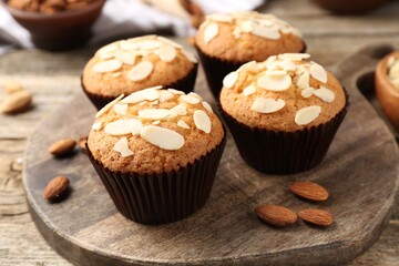 Tasty muffins with almond flakes and nuts on wooden table, closeup
