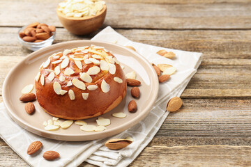 Tasty roll bun with almond flakes and nuts on wooden table, closeup. Space for text