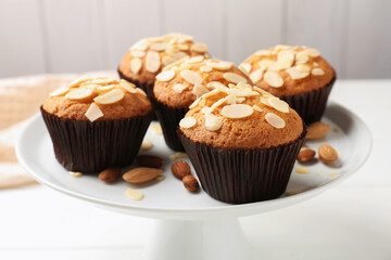 Tasty muffins with almond flakes and nuts on white wooden table, closeup