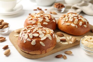 Tasty roll buns with almond flakes, nuts and tea set on white wooden table, closeup