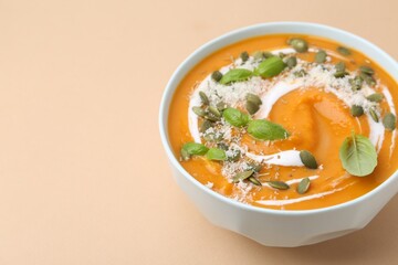 Delicious pumpkin soup with spices, cheese and sour cream in bowl on beige table, closeup. Space for text