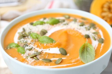 Delicious pumpkin soup with spices, cheese and sour cream in bowl on table, closeup