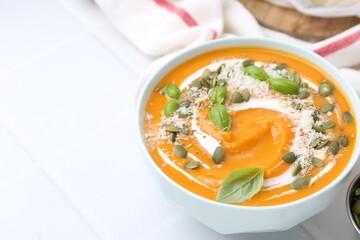 Delicious pumpkin soup with spices, cheese and sour cream in bowl on white tiled table, closeup. Space for text