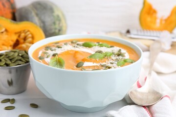 Delicious pumpkin soup with spices, cheese and sour cream in bowl served on table, closeup