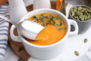 Taking delicious pumpkin soup with spoon from bowl on table, closeup