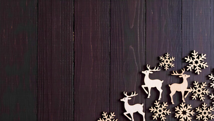 Winter Background with Deer. Wooden deer figurines and snowflakes against a dark wooden background.