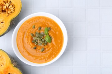 Delicious pumpkin soup in bowl and vegetables on white tiled table, flat lay. Space for text