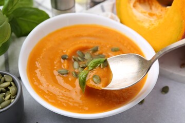 Taking delicious pumpkin soup with seeds and basil from bowl on table, closeup