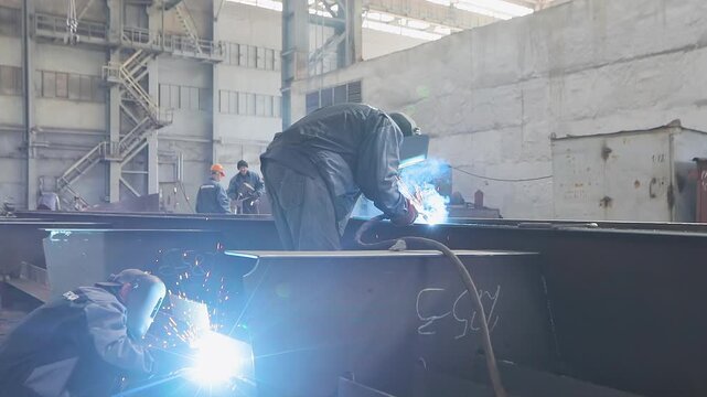 Welders welding large steel sections steel box girder of bridge. Welders weld large steel sections of a bridge's box girder. Box girder steel bridge. Manufacturing plant and Shipbuilding, inside.