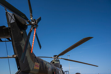 A military helicopter with a red strap attached to its tail. The strap is likely used for identification or to secure the tail during flight. The helicopter is parked on the ground