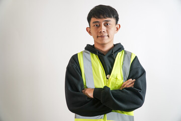 Young man wearing a high visibility safety vest, arms crossed, standing against a white background, portrait