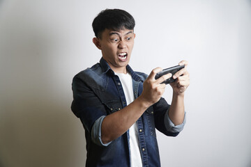 Frustrated young Asian man showing an intense, angry expression while losing a competitive video game on his smartphone