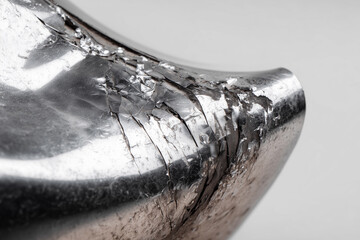 close-up of bent and dented car fender due to accident, metallic texture with scratches, white background