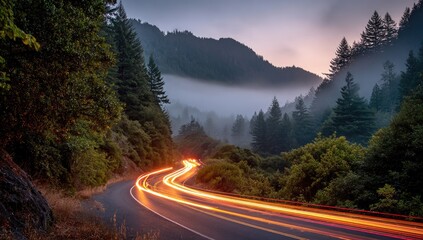 Winding road through a forest at dusk with car light trails leading towards misty mountains