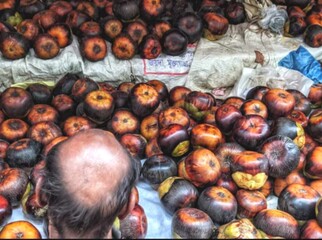The image shows a man standing in front of a market stall filled with Asian palmyra fruits (toddy palms). The fruits are ripe, with shades of dark brown and orange, neatly piled on top of white cloths
