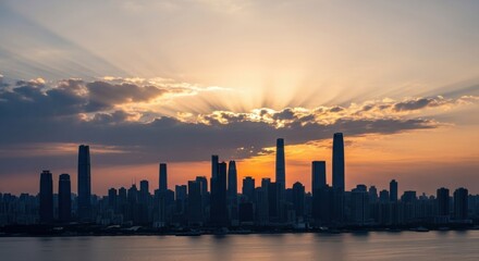 Fototapeta premium Dramatic Sunset Over City Skyline, Sunburst Through Clouds, Silhouetted Buildings.