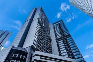 Obraz premium modern office building. Modern skyscrapers with glass and concrete facades rise against a bright blue sky with scattered clouds, showcasing urban architecture and city development.