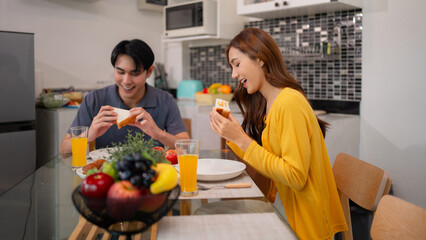 Asian adult couple shares happy morning breakfast meal home kitchen daily routine togetherness...