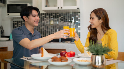 Asian young adult couple enjoy breakfast home kitchen toast orange juice celebrate morning happy healthy lifestyle togetherness relationship