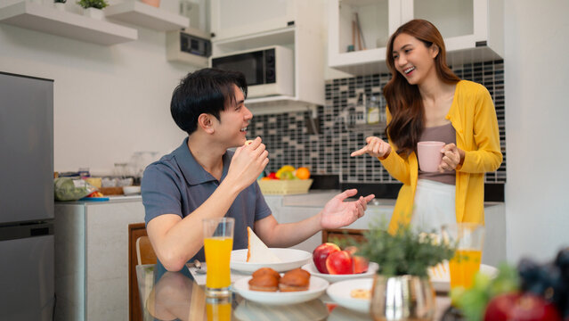Asian young adult couple enjoy breakfast morning meal home kitchen happy conversation bonding together shared food domestic life cozy moment