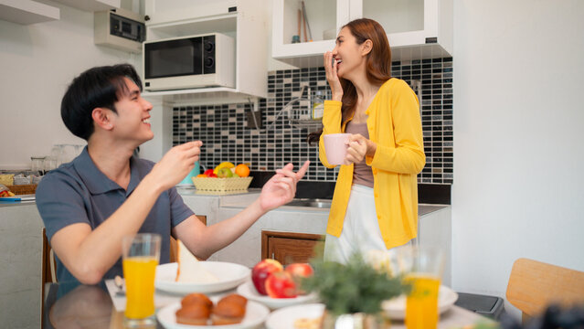 Asian adult couple share breakfast meal together laughing talking happy interaction modern kitchen home domestic lifestyle morning routine