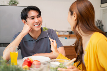 Asian adult couple sharing healthy meal home kitchen dining eating fresh salad bonding relationship...