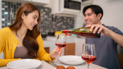 Asian couple shares romantic evening pouring wine happy adult partners enjoy dinner home kitchen intimate moment love celebration at apartment
