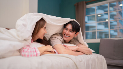 Asian adult couple share happy moment lying in bed under warm blanket cozy bedroom intimate home...